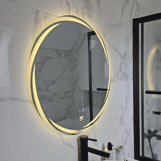 Miroir LED anti-buée Nelsmann Aura en lumière ambrée, à côté d'un pare-douche noir dans une salle de bain en marbre